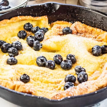 Dutch baby pancake recipe after removing from the oven and topping with fresh berries and powdered sugar.