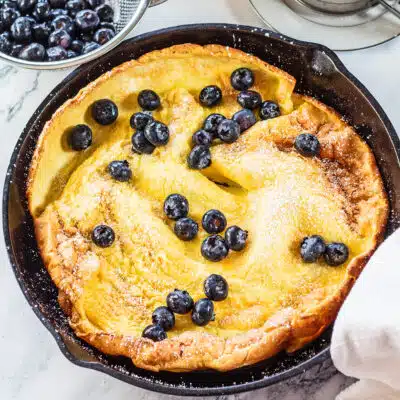 Dutch baby pancake baked to puffy golden perfection and served with confectioners sugar and fresh blueberries in cast iron skillet.