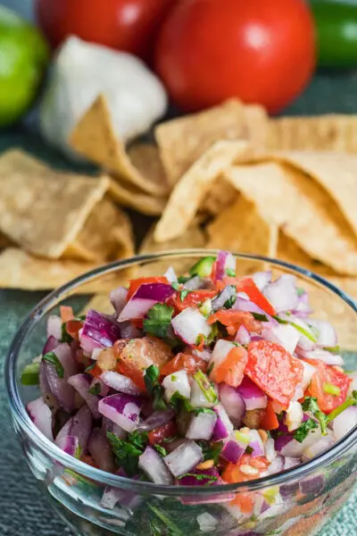 tall angled overhead image of pico de gallo with chips and fresh vegetables.