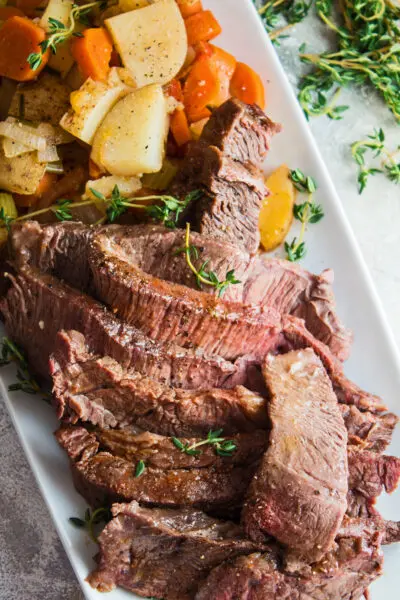tall vertical image of the crockpot yankee pot roast served on a white plate with sliced meat at the front and the vegetables stacked behind