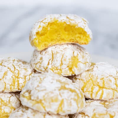 Biscoitos supermacios de cream cheese e limão, empilhados com uma mordida mostrando o centro amarelo do biscoito superior.