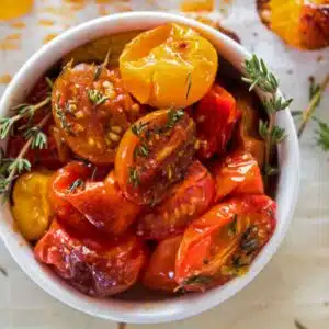 Square image of a white bowl filled with roasted cherry tomatoes.