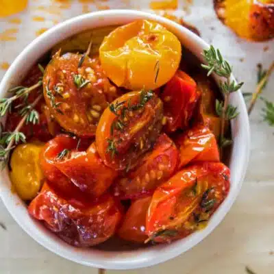 Square image of a white bowl filled with roasted cherry tomatoes.