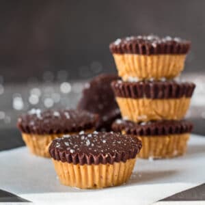 large square sideview image of dark chocolate almond butter cups with one at the front and several stacked behind with grey background