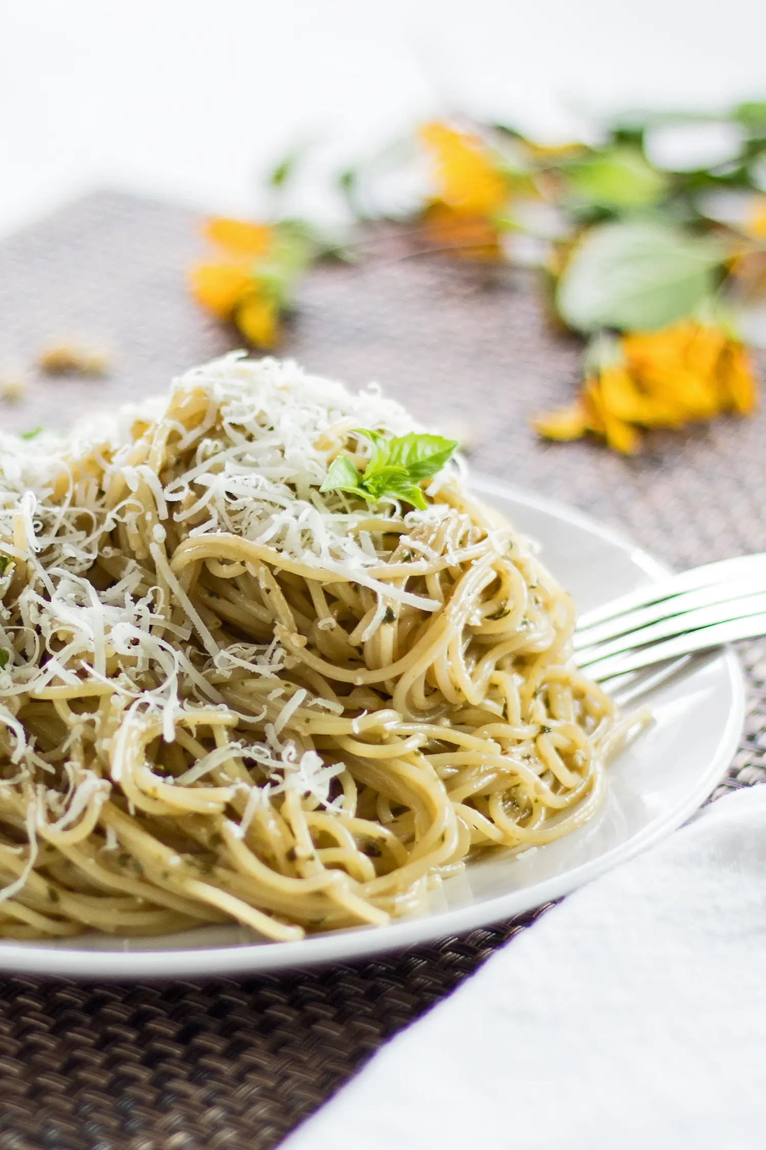 closeup vertical image of basil pesto pasta served on a white plate with brown background