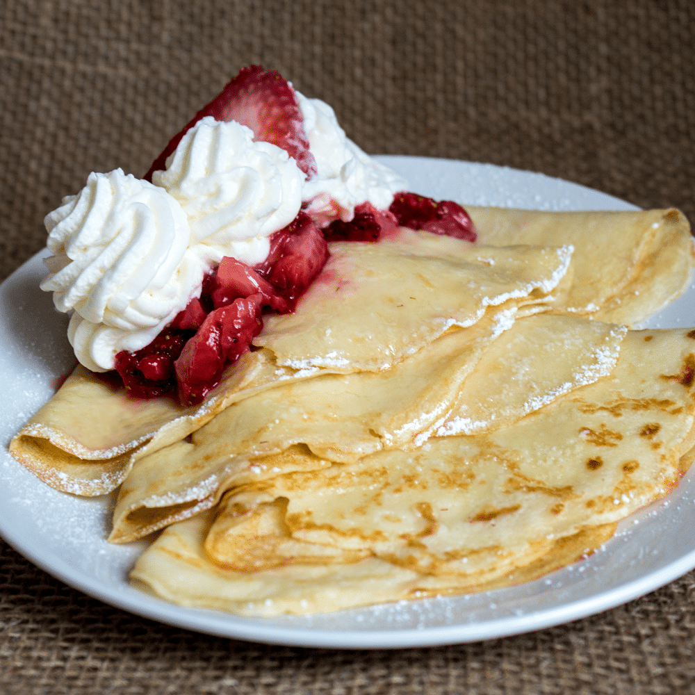 Strawberry buttermilk crepes plated with fresh strawberries and cream.