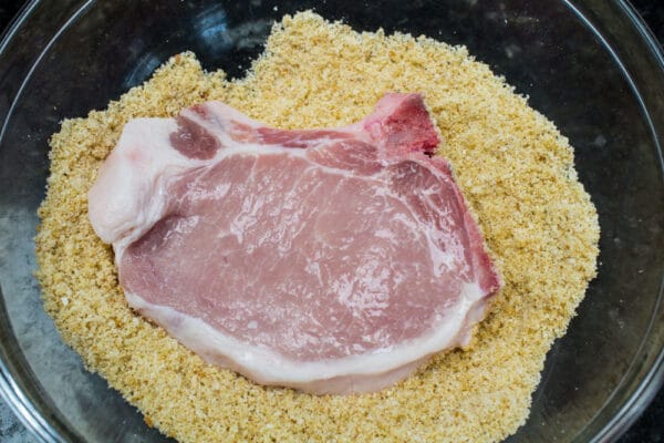 pork chop rinsed and being coated with the breadcrumb mixture before transferring to a baking sheet