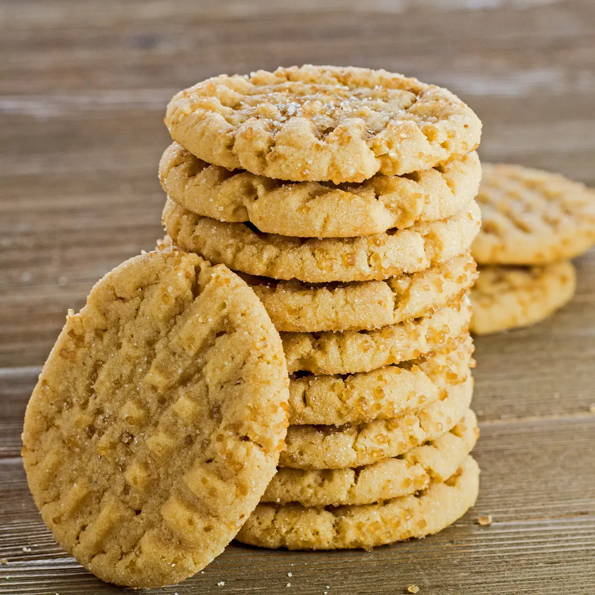 large square image of these tasty almond butter cookies stacked eight cookies high with one tilted against the front of the stack on the left with medium brown wooden background