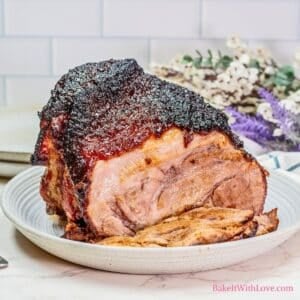 A square image of a brown sugar and Dijon-crusted pork roast sliced on a plate with flowers in the background.