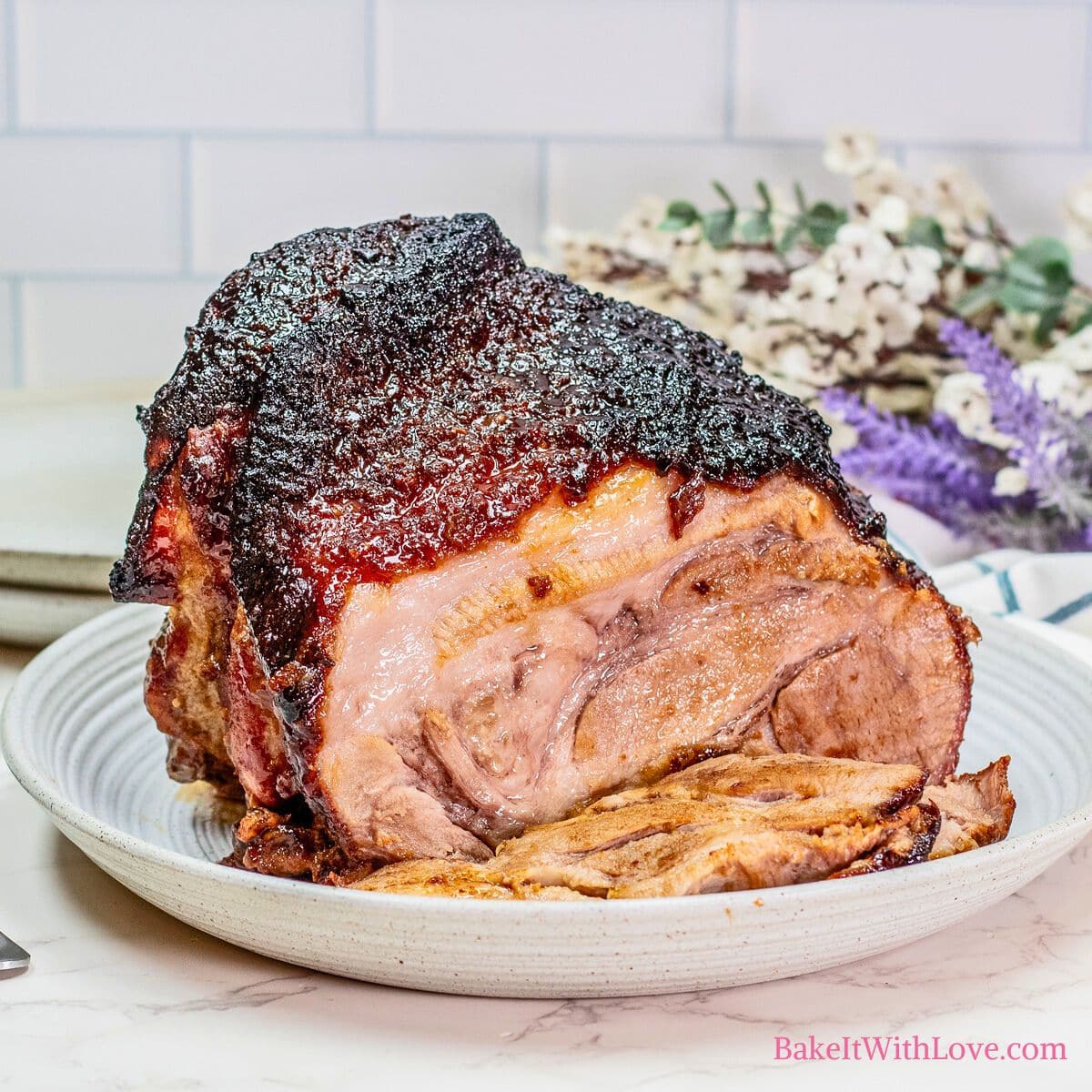 A square image of a brown sugar and Dijon-crusted pork roast sliced on a plate with flowers in the background.