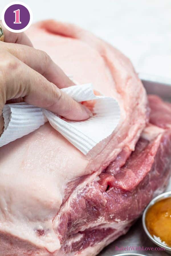 Brown sugar dijon pork roast process 1 showing a hand drying patting the raw roast dry with a paper towel.