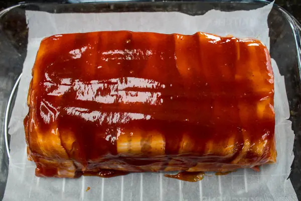 bacon wrapped meatloaf formed and topped with ketchup glaze and ready to be oven baked