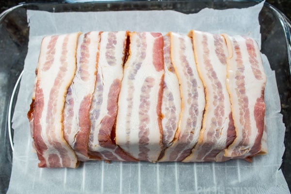 bacon wrapped meatloaf transferred on parchment paper to a rack in a baking dish