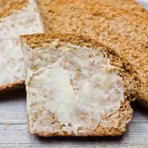 Square image of sliced whole wheat bread with butter.