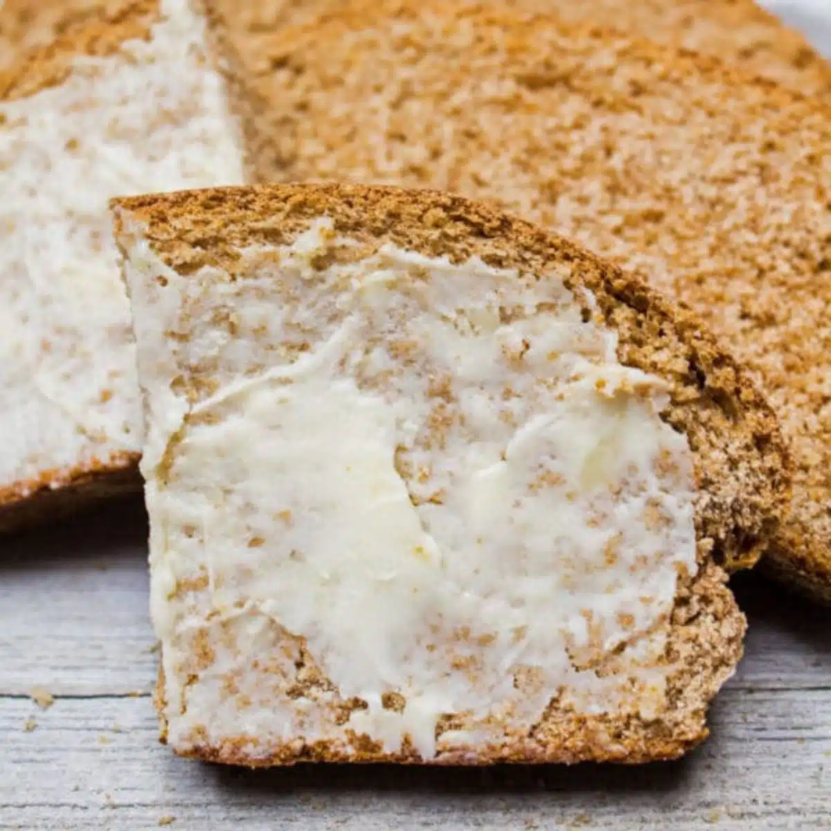 Квадратно изображение на нарязан пълнозърнест хляб с масло.