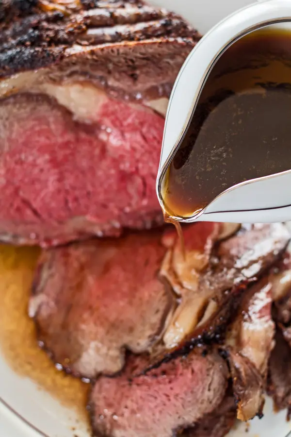 tall image of prime rib red wine au jus being poured over roast beef.
