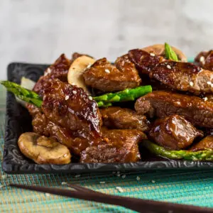 Large square angled view of the left half of the served plate of panda express shanghai angus steak after being wok fried with onion mushroom and asparagus then tossed in the shanghai sauce.
