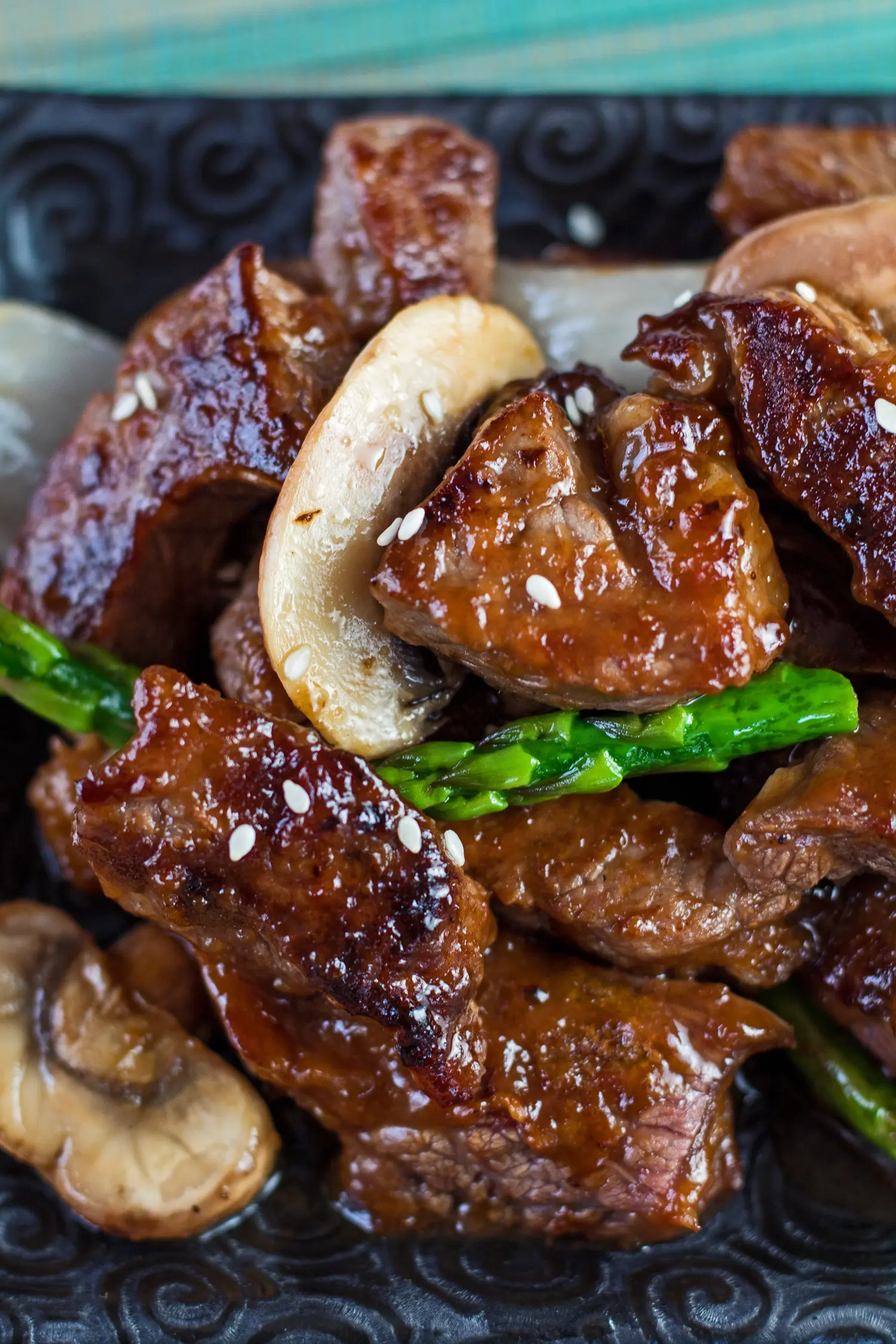 Tall vertical image an angled closeup on the dished panda express shanghai angus steak with pieces of beef onion mushroom and asparagus in sauce and garnished with sesame seeds.