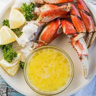 Drawn butter in clear bowl served on white plate with crab legs and lemon wedges.