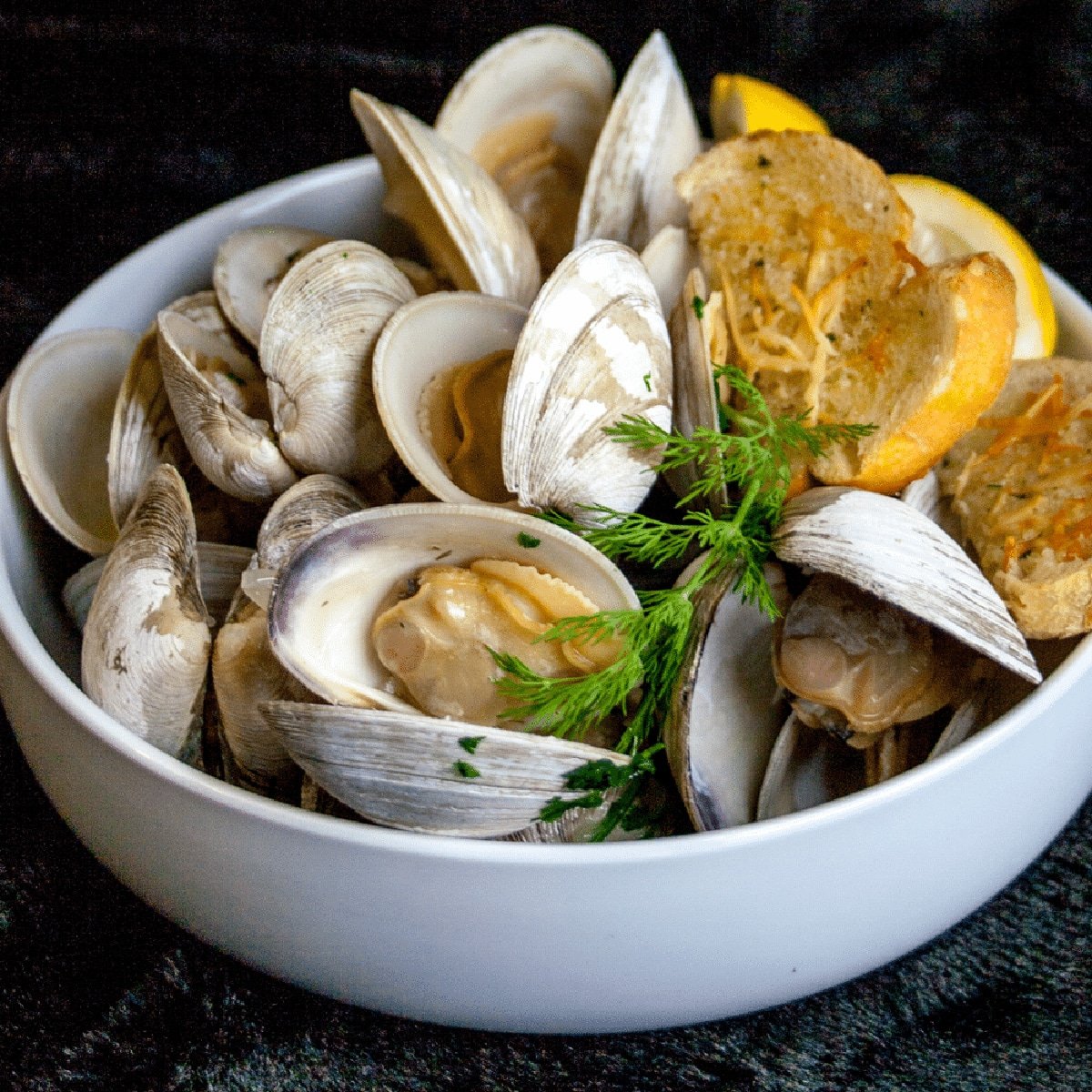 White bowl full of steamed clams with garlic bread.