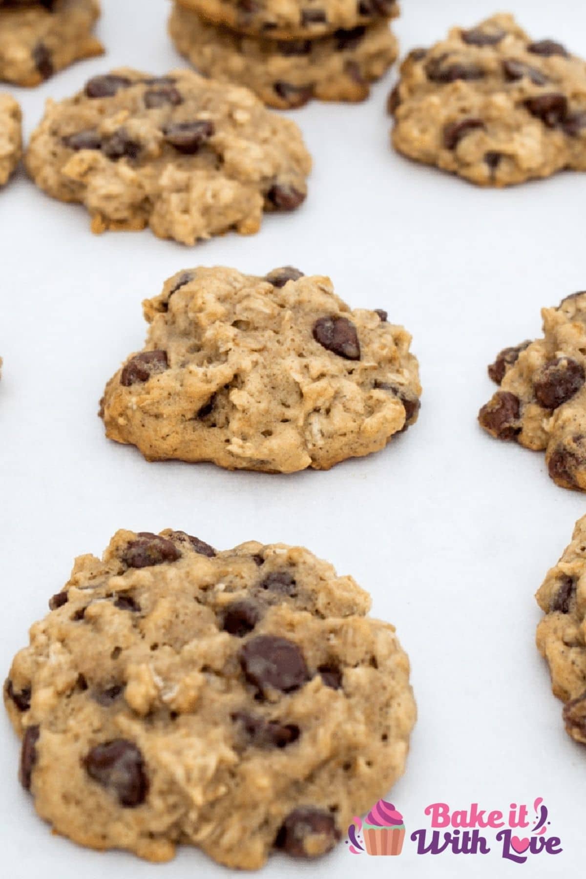 Tall view of the banana oatmeal chocolate chip cookies laid out and stacked on white background.