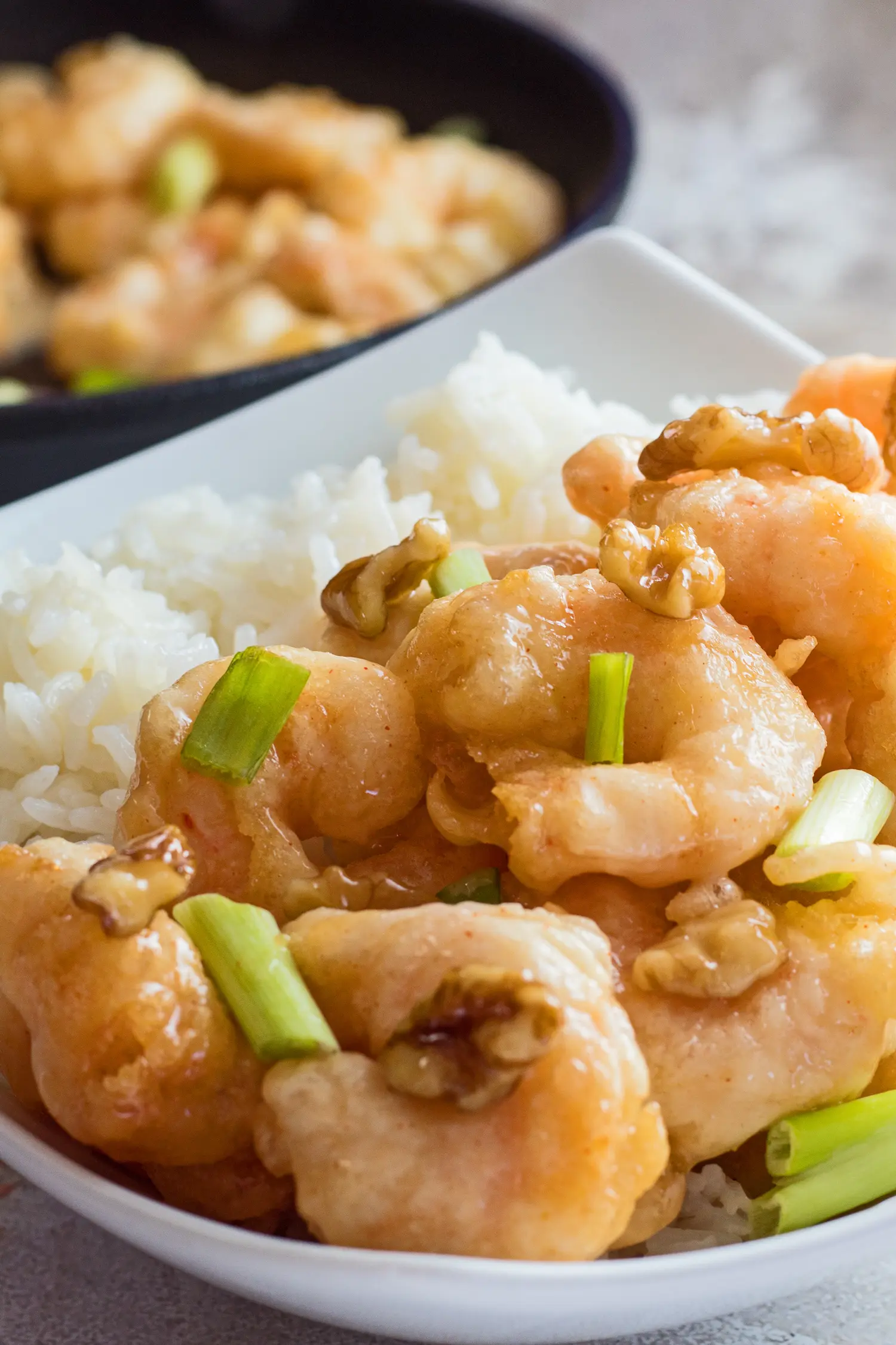 large vertical close up image of the panda express honey walnut shrimp served in a white bowl with green onions as garnish