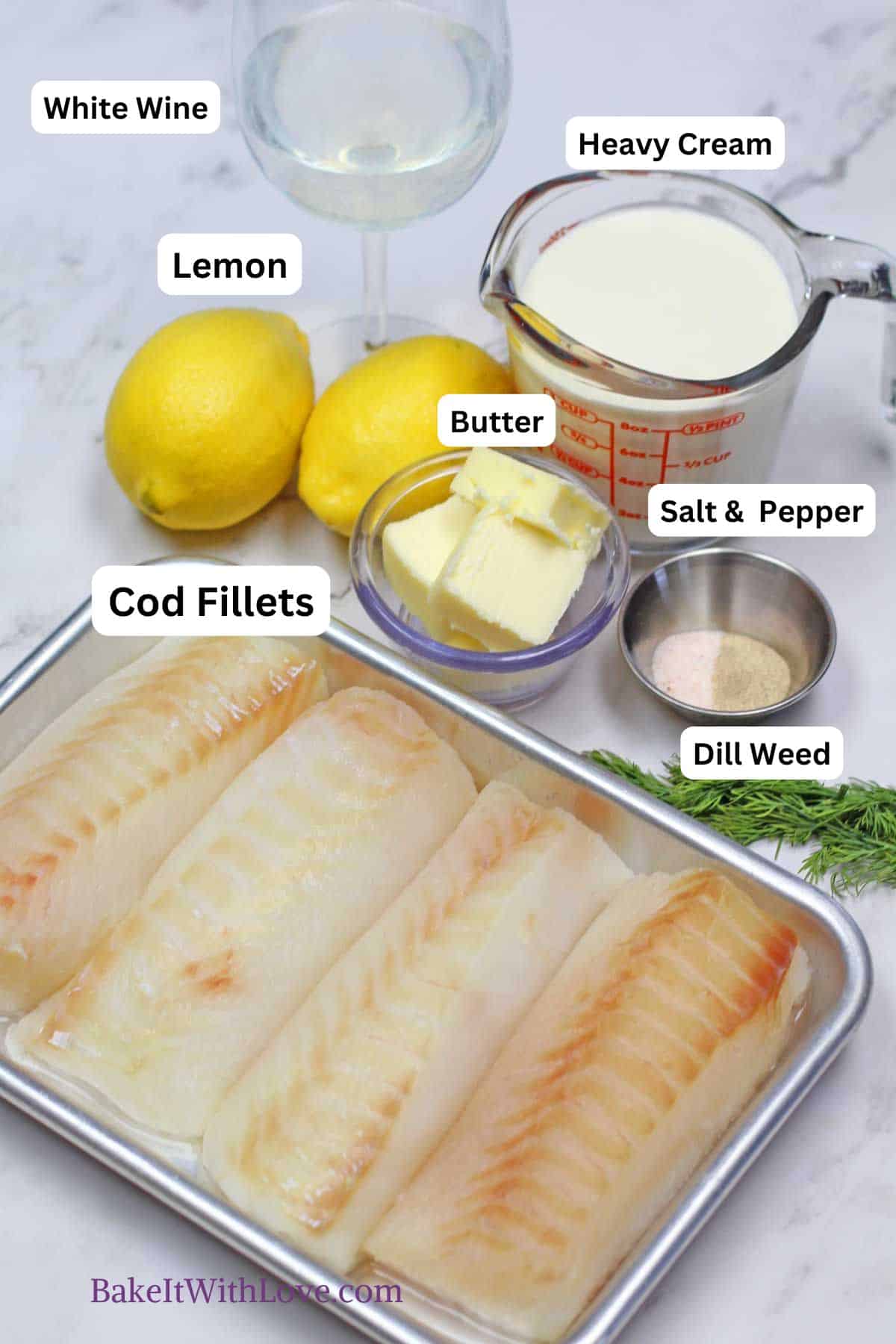 A top-down shot of ingredients for lemon butter baked cod laid out on a white marble surface. In the foreground, four raw cod fillets are arranged in a rectangular metal baking pan. Behind the pan, labeled ingredients include: "White Wine" in a stemmed glass, "Lemon" next to two whole lemons, "Heavy Cream" in a clear measuring cup, "Butter" (cubed) in a small glass bowl, "Salt & Pepper" in a small metal dish, and "Dill Weed" represented by fresh dill sprigs. The bottom left corner has "BakeItWithLove.com" in purple text.