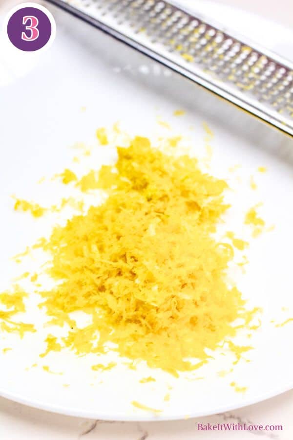 Lemon butter baked cod process photo 3. A bright pile of freshly grated lemon zest, a vivid yellow, rests on a pristine white surface. A portion of a metal grater is visible at the top, implying recent use. The top-left corner features a purple circle with the number "3".