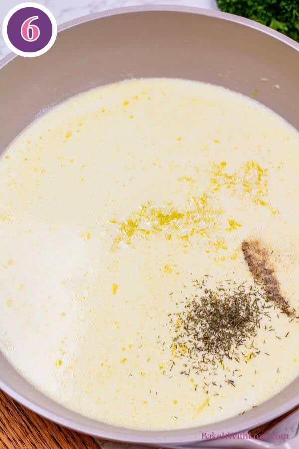Lemon butter baked cod process photo 6. A wide, light-colored pan holds a simmering pale yellow liquid, dotted with melted butter, fine yellow zest, and a darker cluster of herbs. The surface of the liquid shows slight ripples. The top left features a purple circle with the number "6".