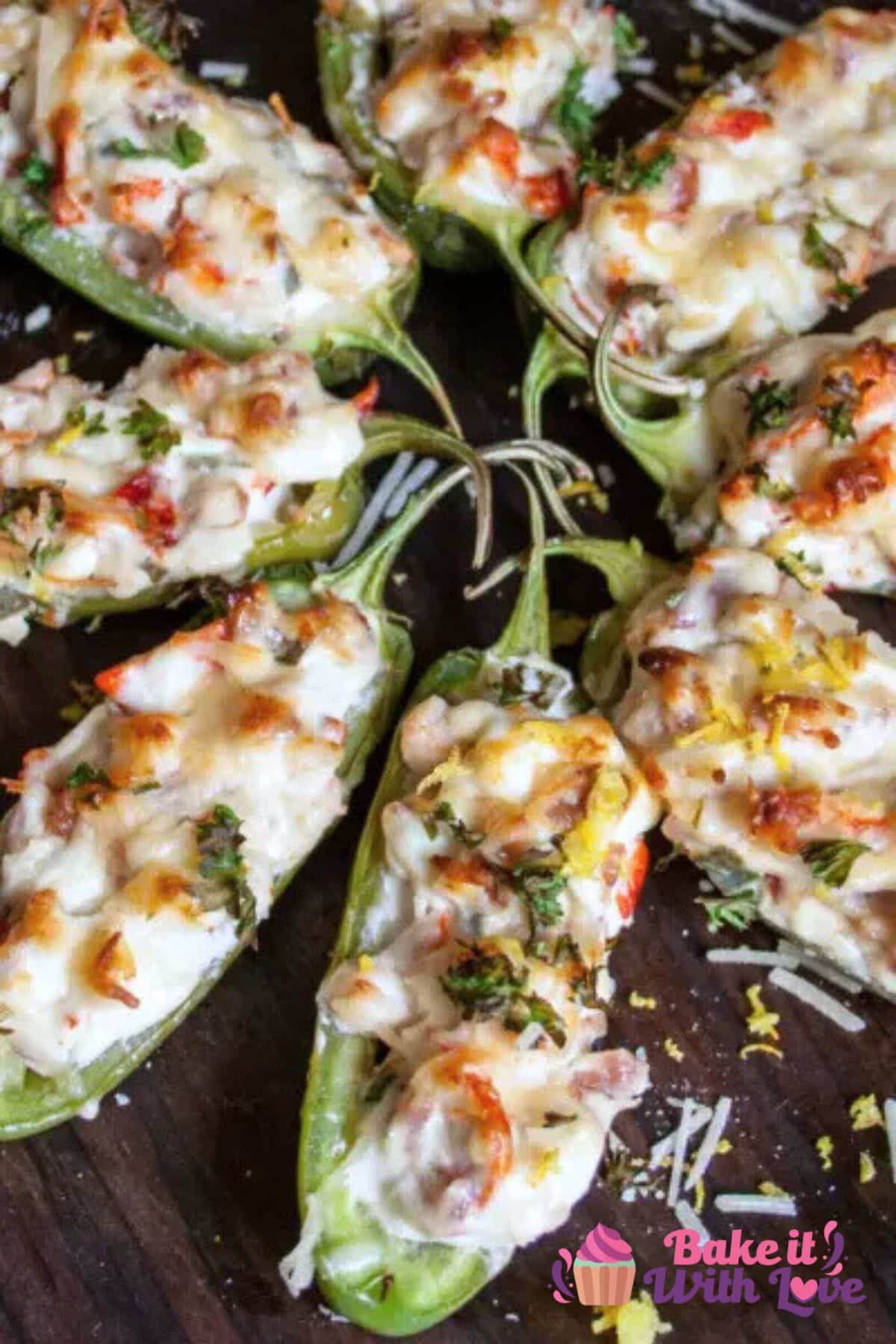 A tall image showing a top-down view of eight lobster jalapeño poppers displayed in a starburst pattern on a dark wooden background. Each jalapeño half is filled with a rich lobster and cheese mixture, melted and golden on top, and garnished with chopped herbs, Parmesan, and lemon zest.