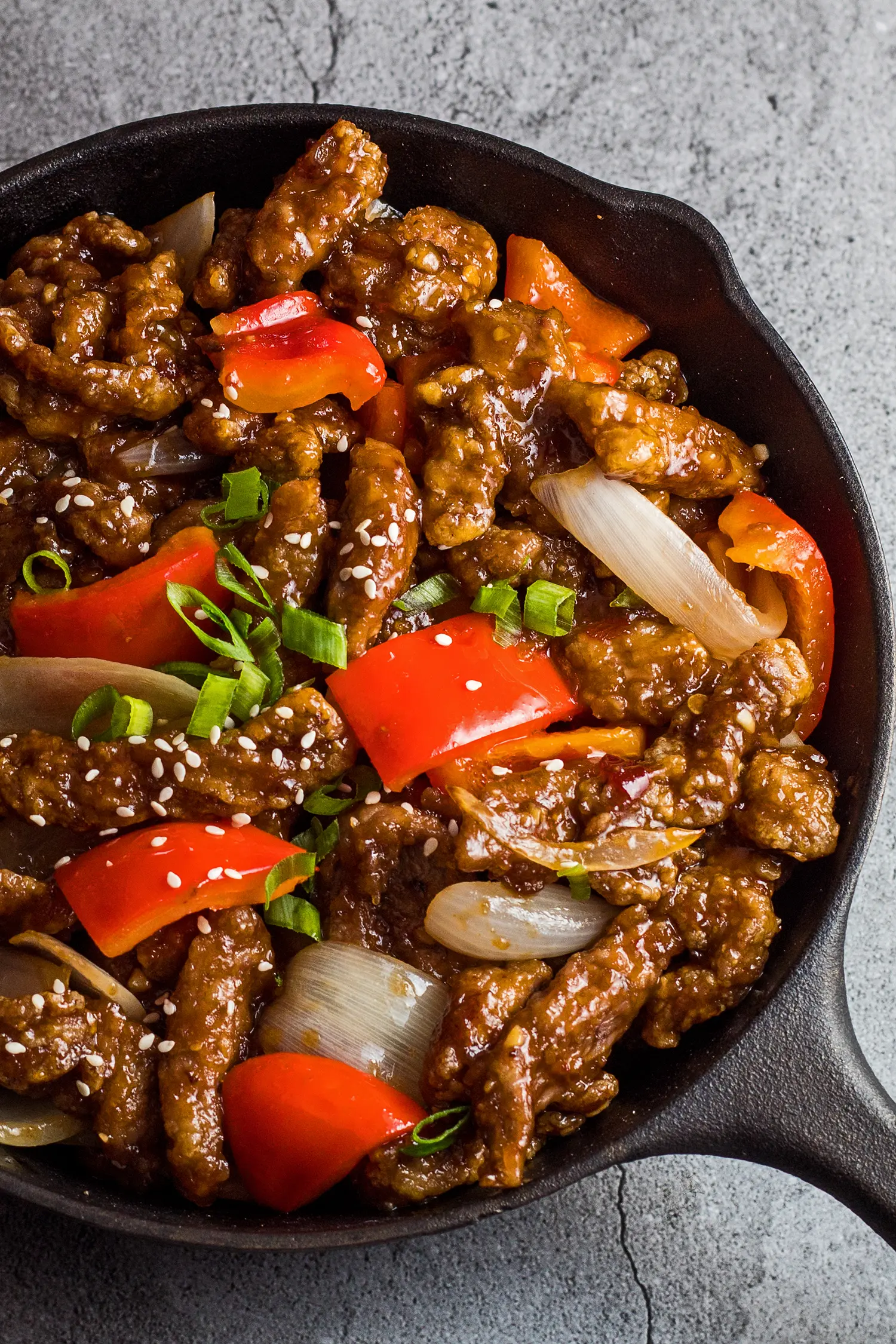 Tall overhead photo of the beijing beef in the pan garnished with green onion and sesame seeds.