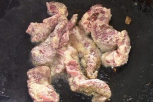 marinated beef strips being wok fried in oil