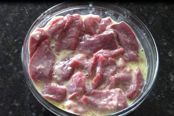 sliced beef being marinated before coating with cornstarch and being wok fried