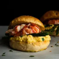An amazing Lobster Breakfast Sandwich piled high with creamy scrambled eggs, asparagus and lobster on a fresh brioche sandwich bun!