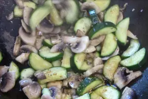 zucchini and mushrooms being stir fried with garlic and ginger added