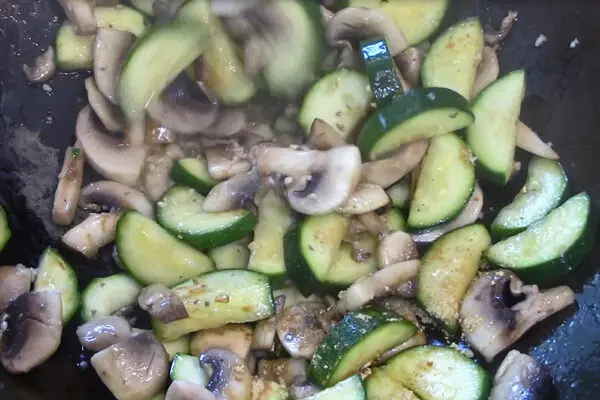 zucchini and mushrooms being stir fried with garlic and ginger added