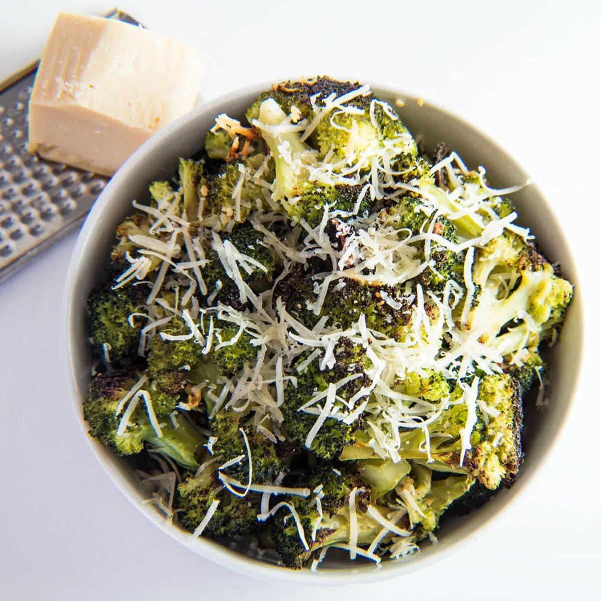 Roasted broccoli in a white bowl with Parmesan on top.