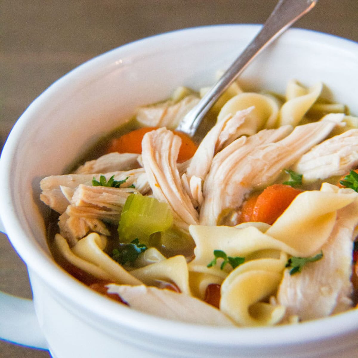 Square image of chicken noodle soup in a white bowl.