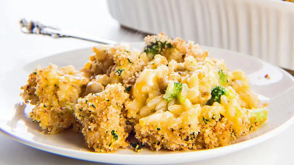 Wide image of a tasty cheesy chicken broccoli rice casserole served on white plate.