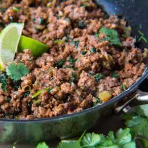 Square image of taco meat in a cast iron pan with a lime wedge.
