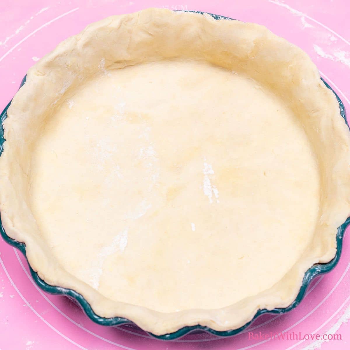 A square image of an all-butter pie crust spread in a pie dish sitting on a pink baking mat.