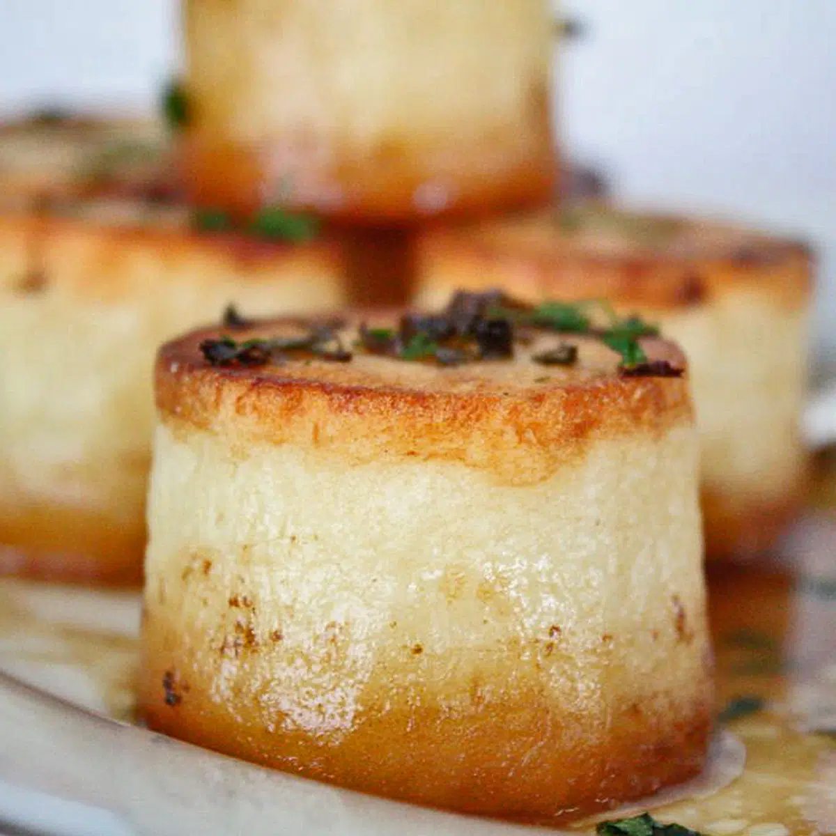 Fondant potatoes served on white tray with pan juices.
