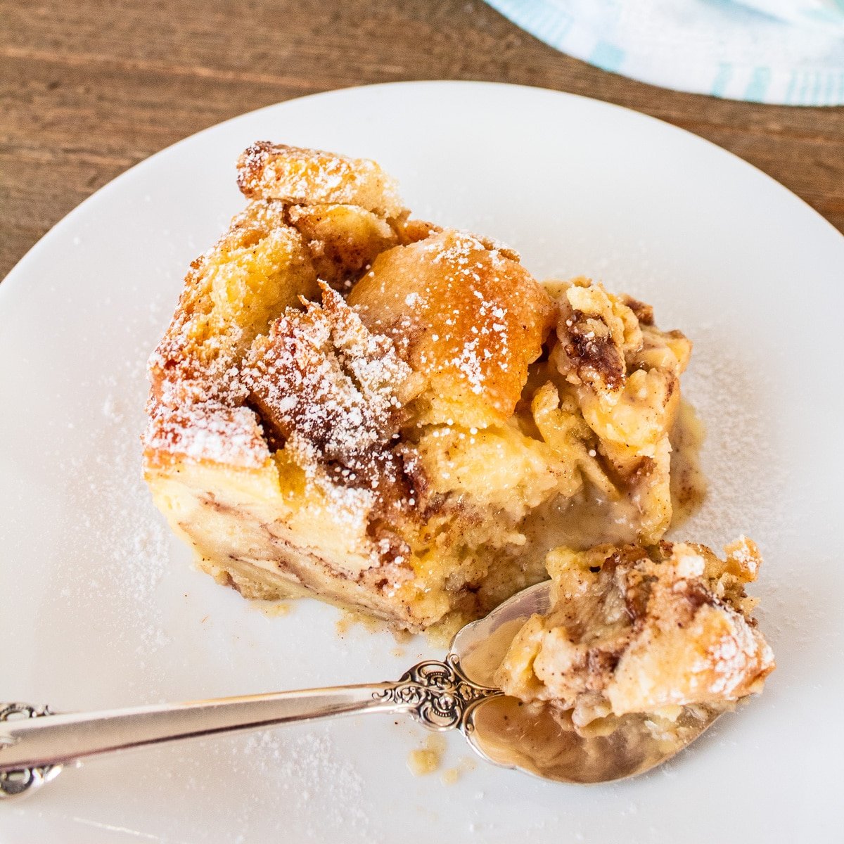 Tasty cinnamon roll bread pudding sliced and served on a white plate and dusted with powdered sugar.