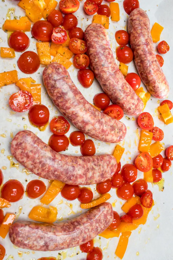 Italian sausages being prepared for baking, with cherry tomatoes and bell peppers.