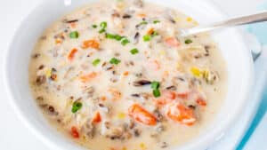 Creamy chicken minnesota wild rice soup in white soup bowl with spoon dipped into the bowl.