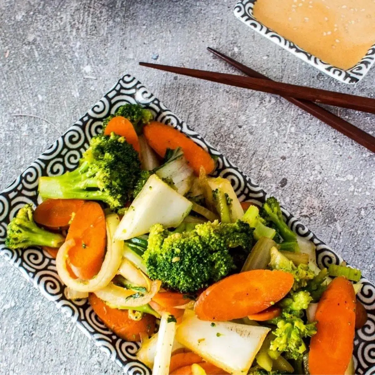 Square image of hibachi vegetables on a grey background with chopsticks.