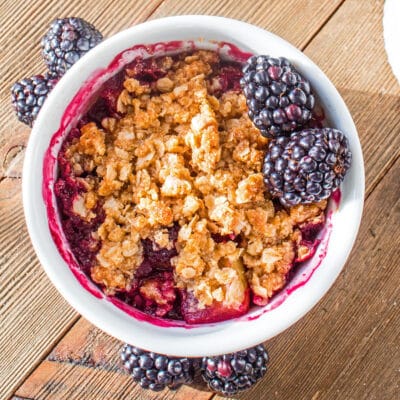 Large square image of blackberry apple crumble in a white bowl.