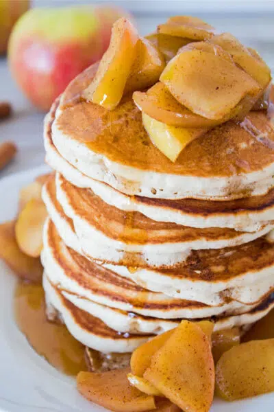 Apple cider pancakes stacked on a white plate.