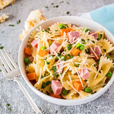 Snabb och enkel ostliknande skinkpasta är full av rejäla smaker från den läckra skinkan, ärtorna och morötterna och ostsås serveras med bowtie-pasta!
