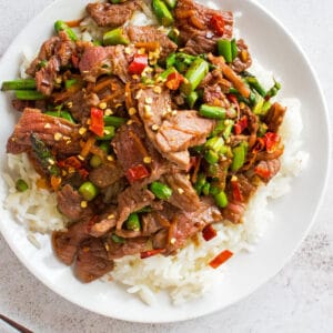 Hunan beef over a bed of white rice, on a white plate.